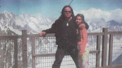 Jarosław Bielan z długimi włosami stoi z córką na tarasie widokowym. Oboje są ciepło ubrani. W tle widać ośnieżone góry i niebo.