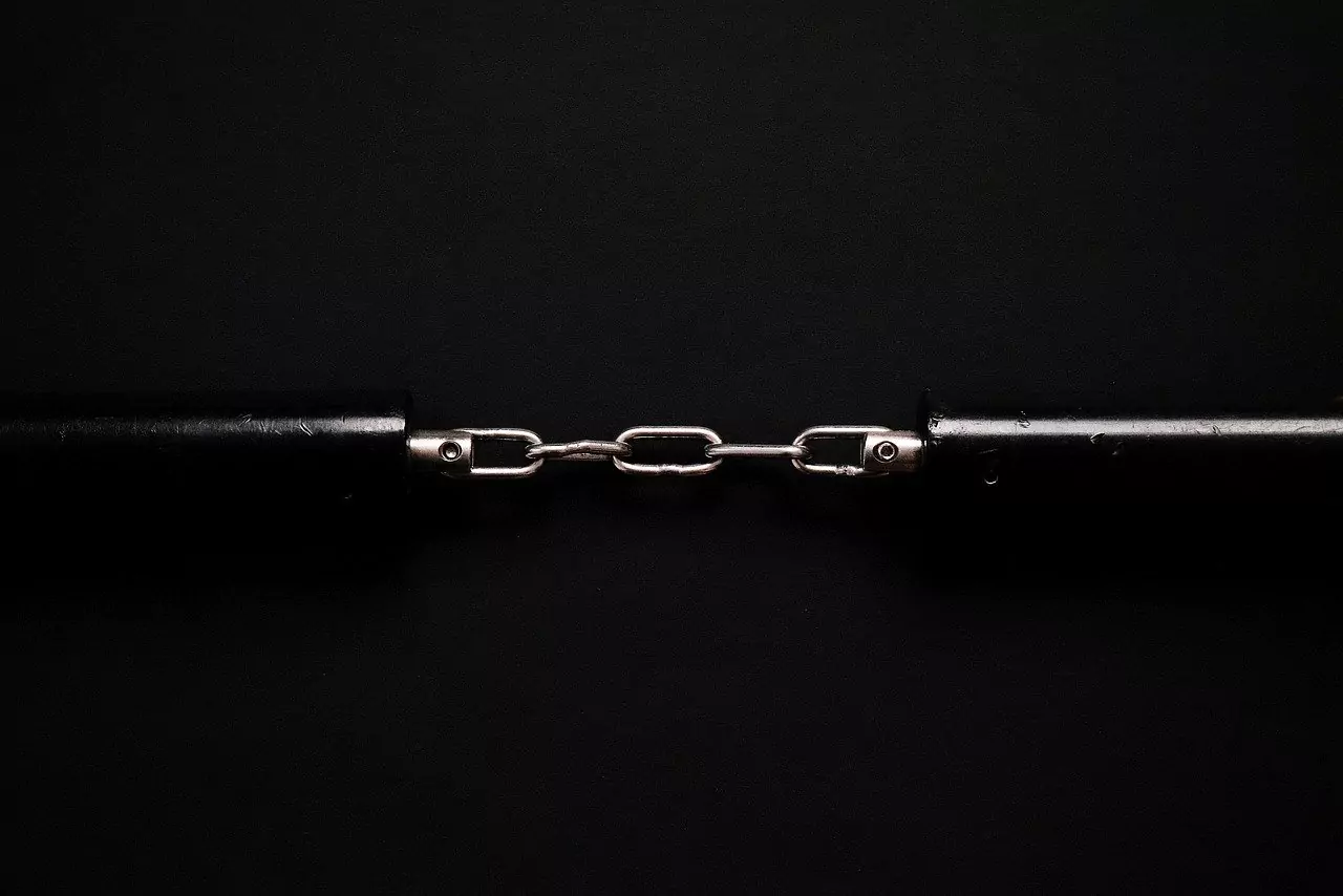 Dwie metalowe liny połączone krótkim łańcuchem, na czarnym tle. Centralny łańcuch trzyma oba końce razem, tworząc symetryczną, minimalistyczną kompozycję.