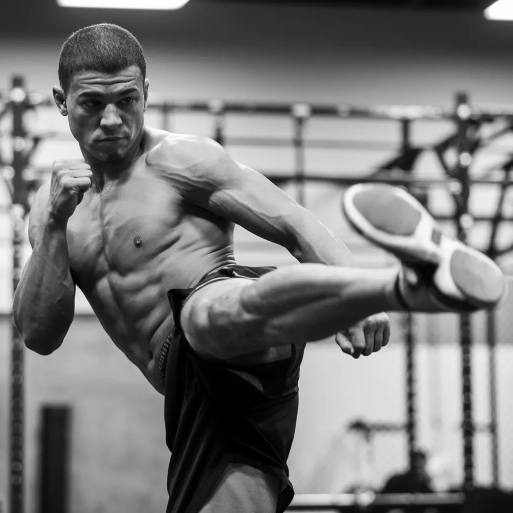 Mężczyzna wykonuje wysoki kop w dynamicznej pozie, intensywnie ćwicząc w siłowni. Tło jest nieostre, ukazując sprzęt do ćwiczeń.