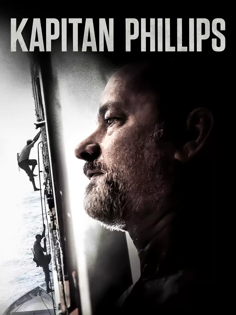Mężczyzna patrzy poważnie przed siebie. W tle dwie postacie wspinają się na burtę statku. U góry widnieje napis "KAPITAN PHILLIPS".