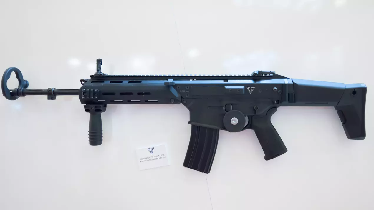 Broń palna w formie karabinu automatycznego spoczywa na białym tle. Pod karabinem znajduje się kartka z napisem: "MSBS GROT C 16 FB-M4 CAL. 5,56 x 45 mm".