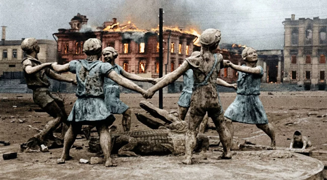 Posągi dzieci trzymających się za ręce tworzą krąg, stojąc wokół krokodyla, w tle płonie budynek. Wokół panuje pustka i zniszczenie.