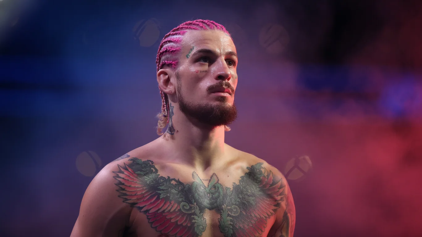 Mężczyzna z różowymi warkoczami patrzy w dal. Tattoo z motywem ptaka na jego klatce piersiowej. Otoczony dymem w kolorach niebieskim i różowym, tworzącym dramatyczny efekt.