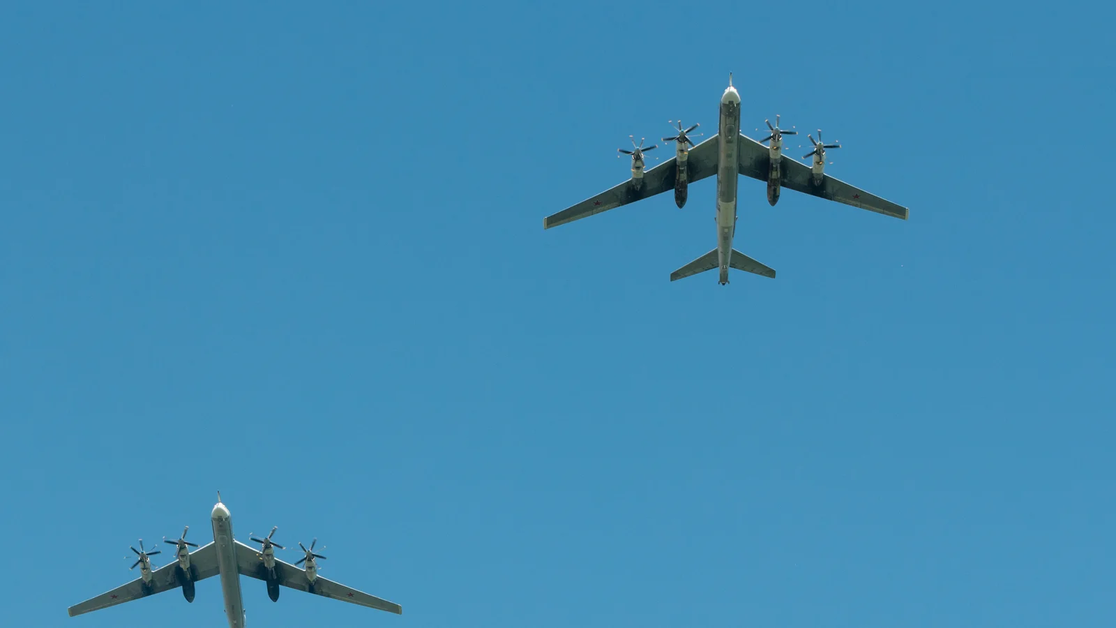 Dwa bombowce Tu-95 widziane od spodu na tle błękitnego nieba, widoczne cztery gondole silnikowe i skośne skrzydła