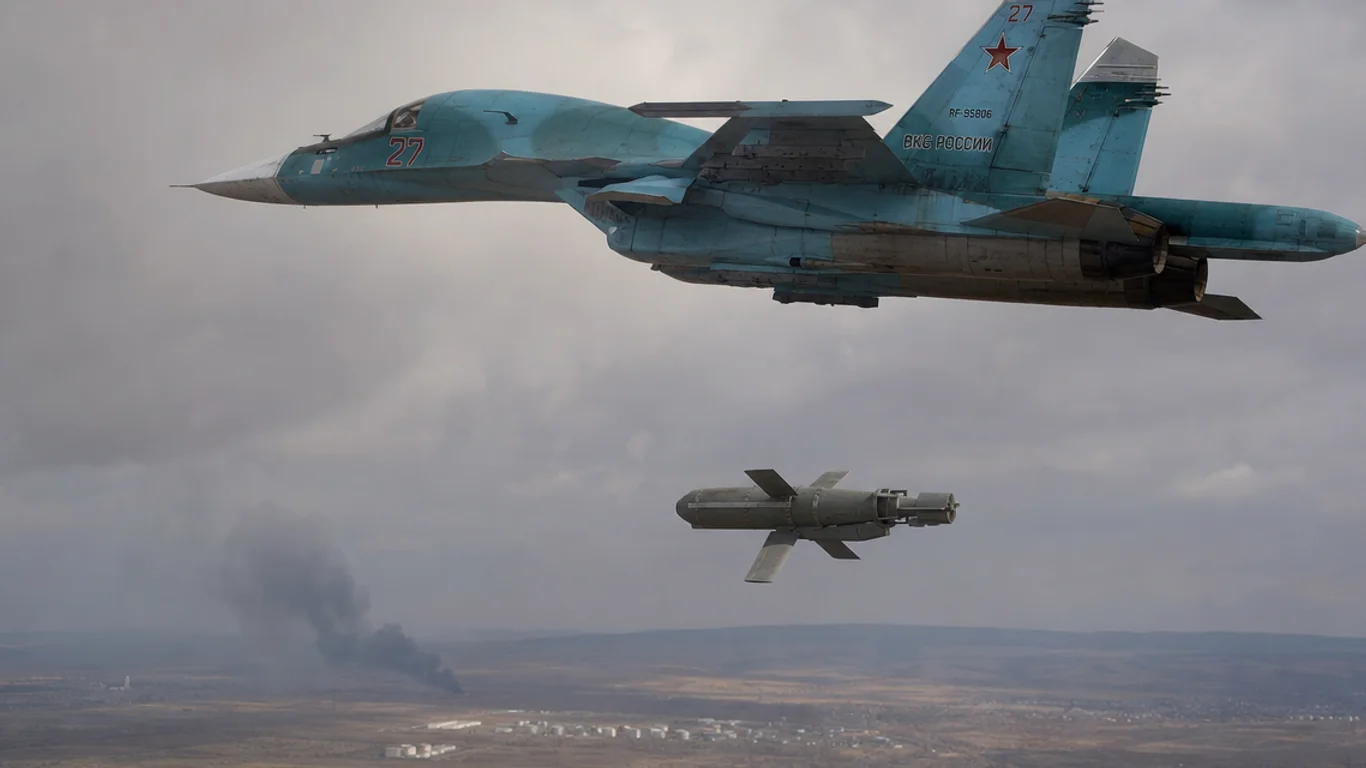 Rosyjski myśliwiec bombardujący Su-34 zrzucający bombę szybującą FAB z rozkładanym zestawem skrzydeł UMPK nad polem walki, widoczny moduł nawigacyjny i powierzchnie sterowe, pochmurne niebo.