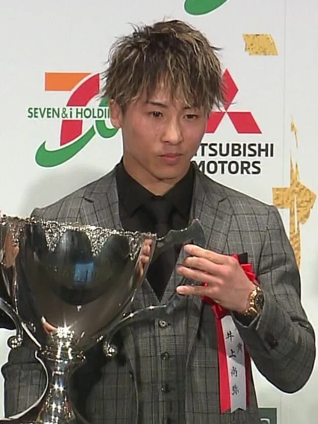Naoya Inoue w garniturze trzyma duży puchar podczas ceremonii wręczenia nagród