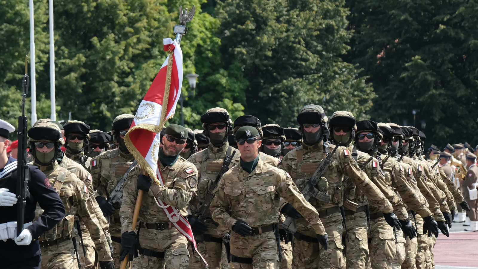 Kolumna żołnierzy JW AGAT w kamuflażu MultiCam maszeruje ze sztandarem jednostki podczas defilady wojskowej