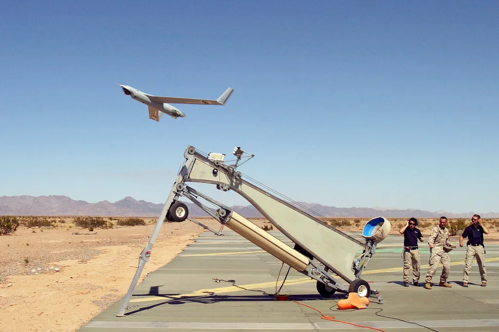 Start bezzałogowca ScanEagle z wyrzutni katapultowej na pustynnym lotnisku, w tle maszyna już w powietrzu