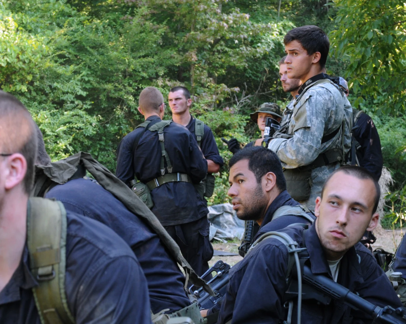 Kandydaci Special Forces w mundurach polowych i partyzanci w czarnych uniformach planujący wspólnie operację w lesie podczas ćwiczenia Robin Sage