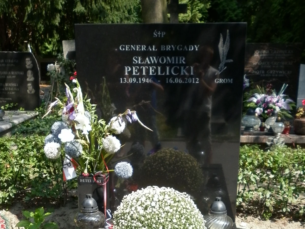 Czarny granitowy nagrobek z napisem Generał brygady Sławomir Petelicki 13.09.1946 – 16.06.2012 i symbolem GROM, pokryty kwiatami i zniczami