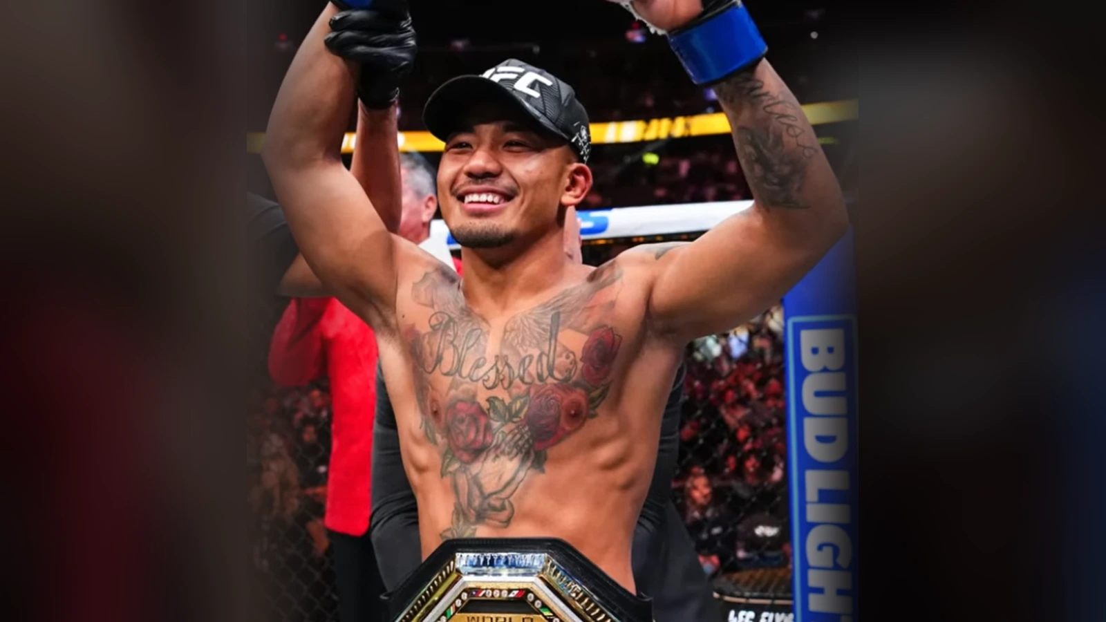 Joshua Van w czapce UFC, z uniesionymi rękami w rękawicach i mistrzowskim pasem wagi muszej w pasie