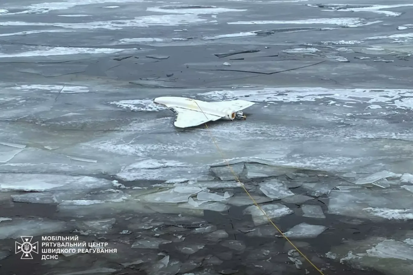 Biały dron w układzie delta leżący na popękanym lodzie zamarzniętego zbiornika, przywiązany liną